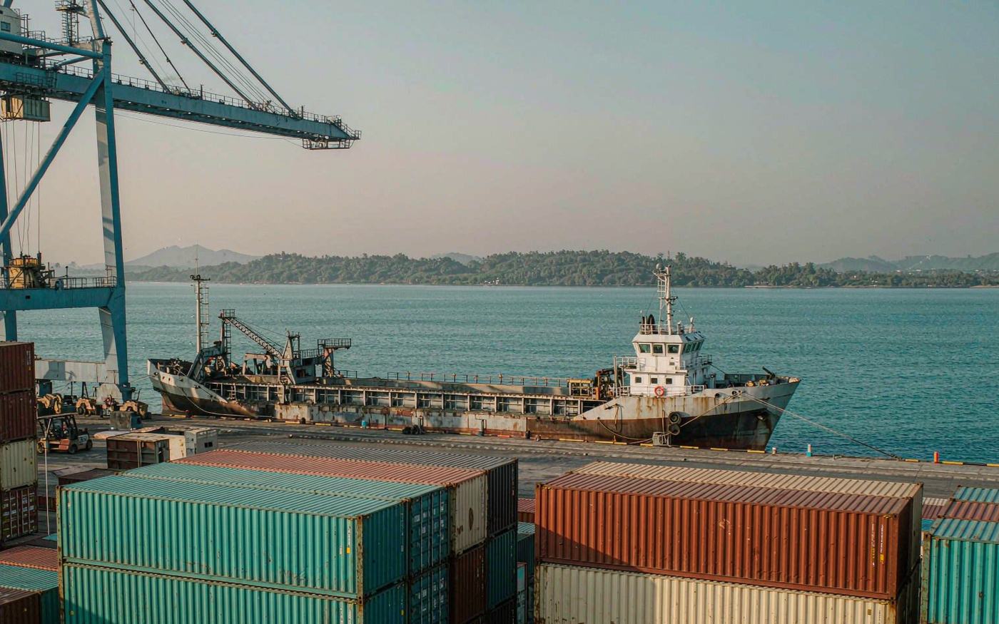 Container terminal at a Caribbean deep-water harbour with a feeder vessel alongside and low green hills behind