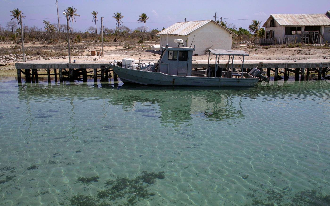 Small arid Dutch Caribbean island harbour with a concrete pier, a feeder vessel alongside, crated cargo and low white buildings behind