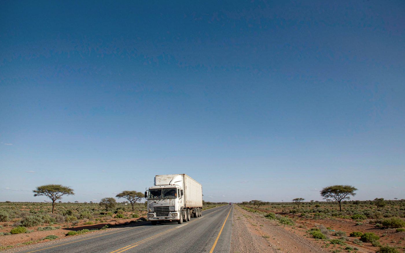 A container truck on a long straight highway across semi-arid Kalahari landscape in Botswana