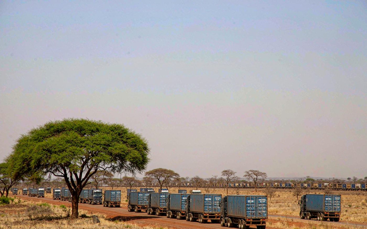 Truck convoy carrying shipping containers on a laterite road across the Sahel towards Ouagadougou