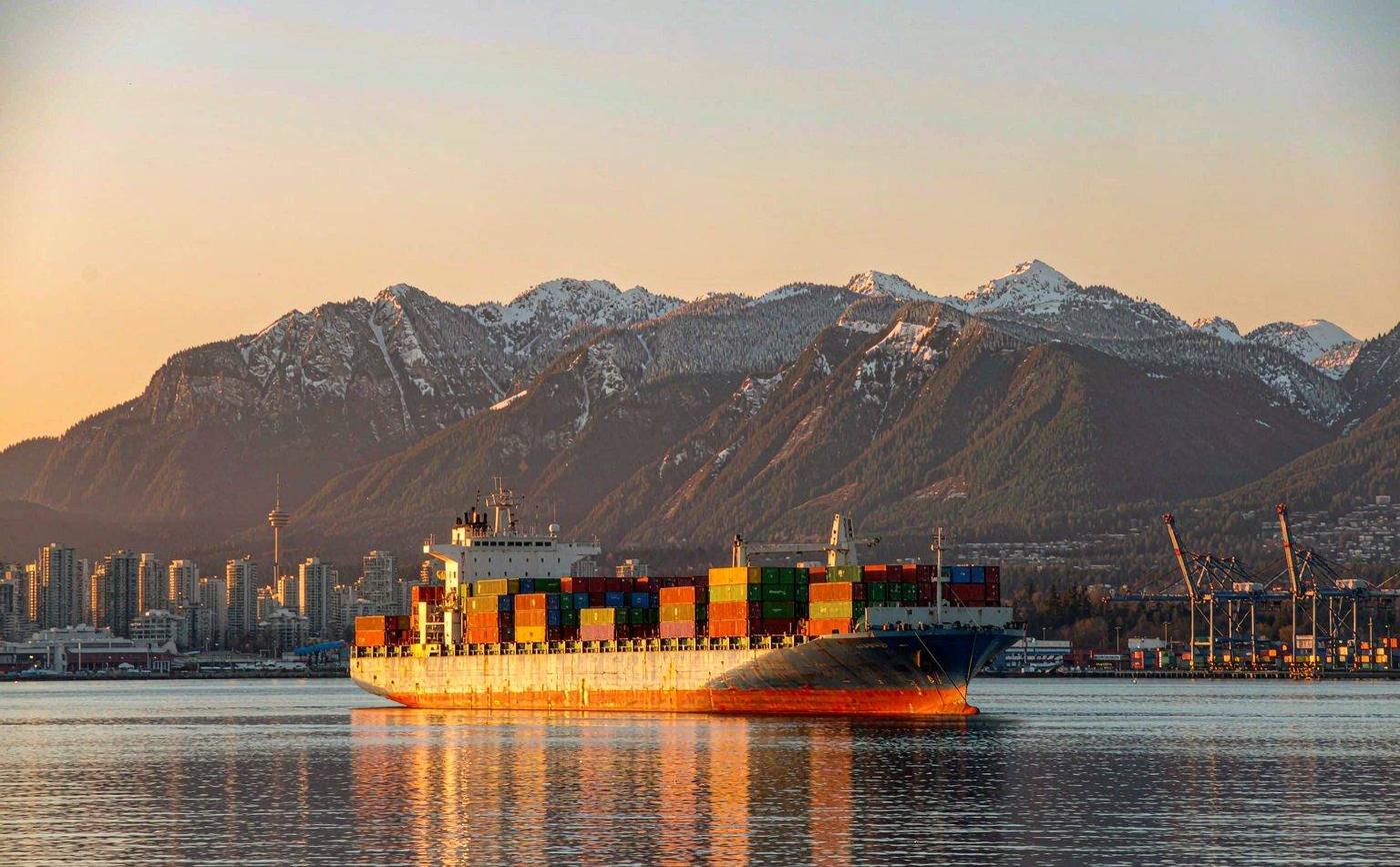Container ship arriving at the Port of Vancouver, Canada, with coastal mountains behind the terminal