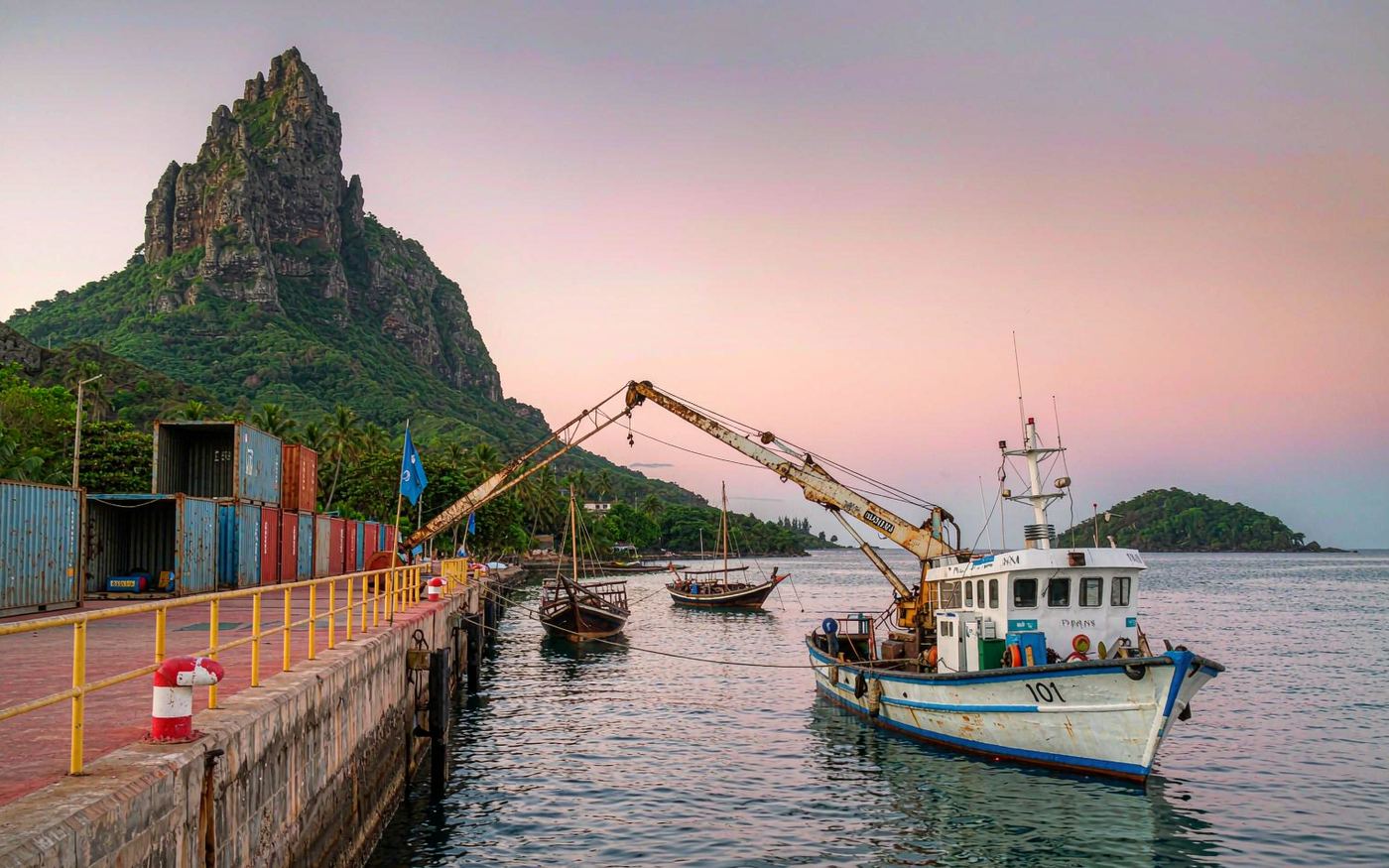 Small harbour of Moroni in the Comoros at sunrise with containers, dhows and volcanic hills behind