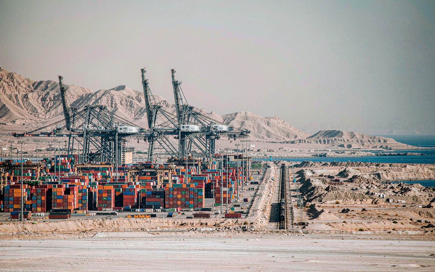 Container terminal on an arid Red Sea coast with a freight train running inland beside the port