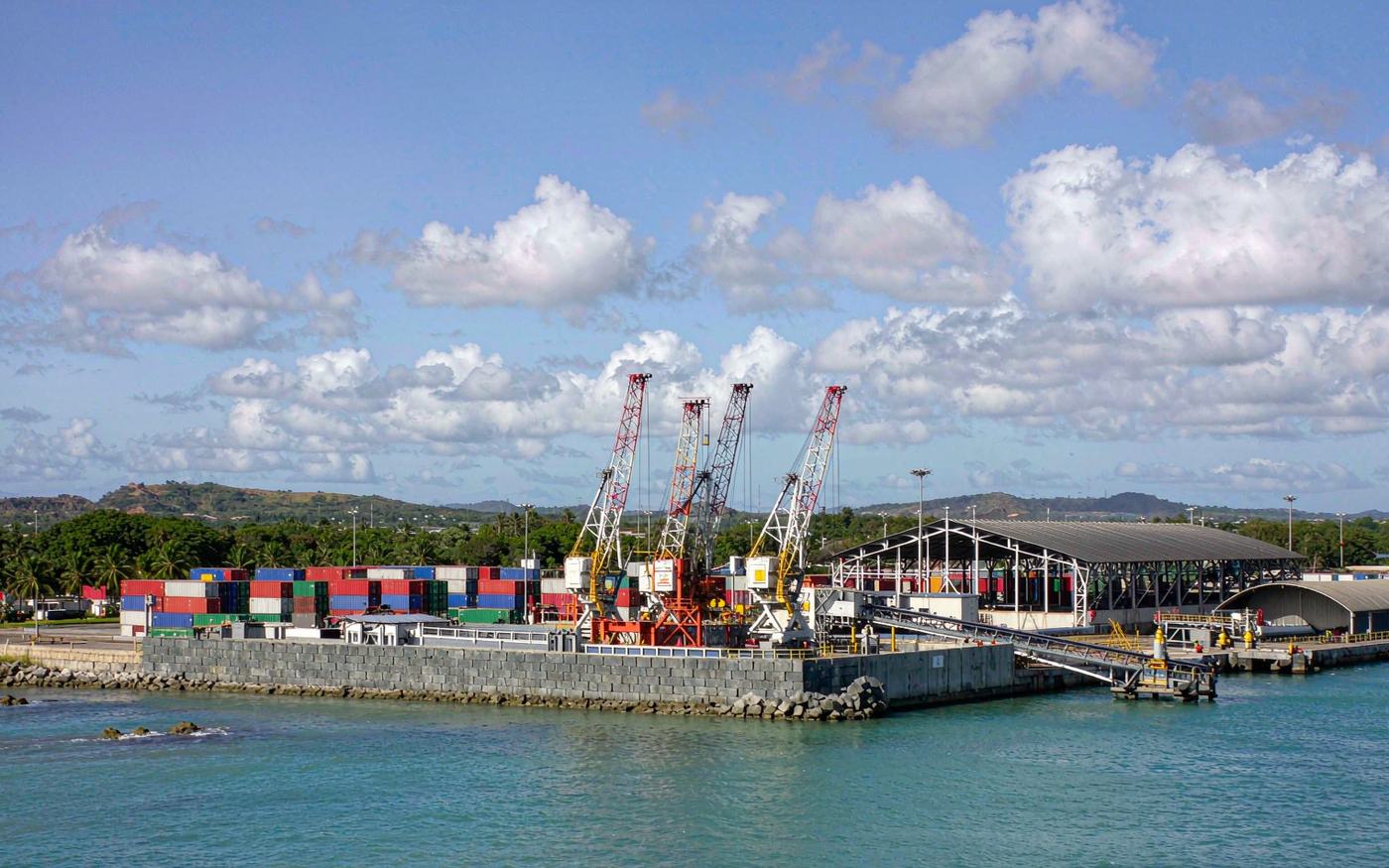 A Caribbean container port with gantry cranes, stacked containers and turquoise water in the foreground