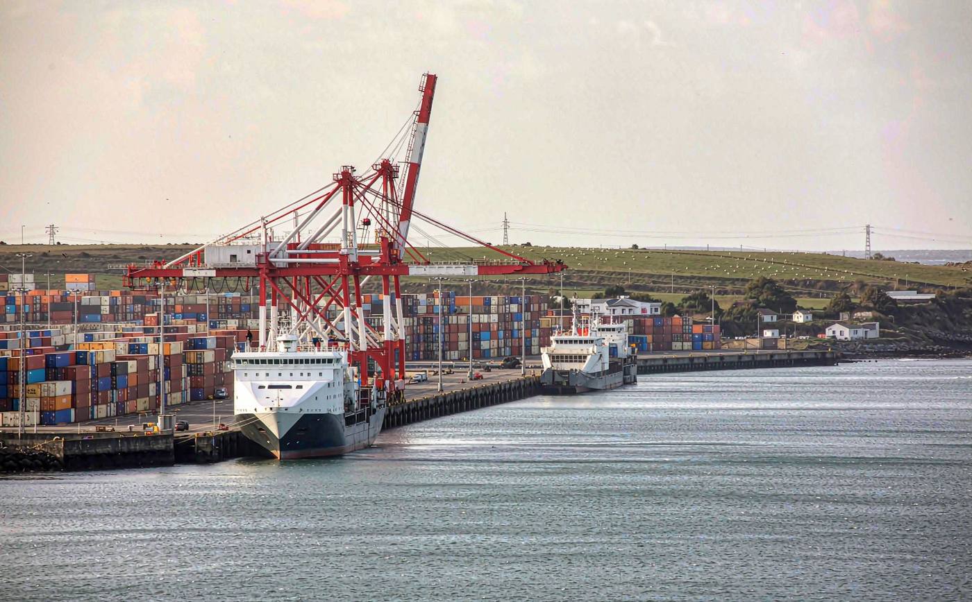 Container terminal on the Irish coast with gantry cranes at the quay, stacked containers in the yard, a vessel alongside and a ro-ro ferry ramp