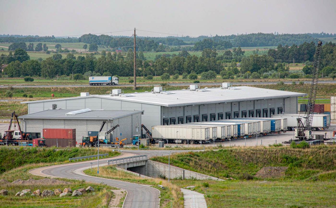Inland logistics park in Western Europe with a warehouse, loading docks, semi-trailers and stacked shipping containers