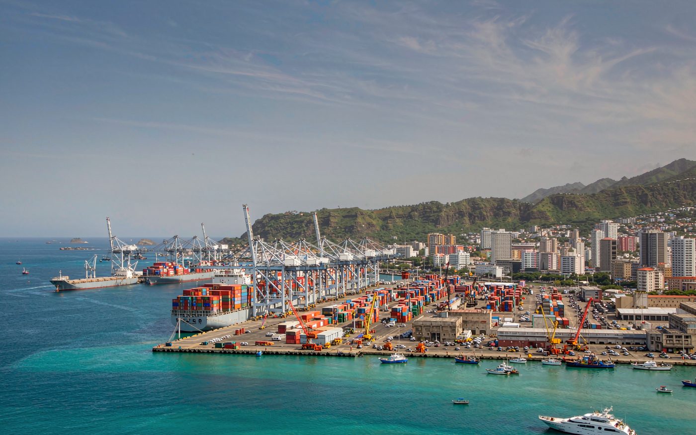 The harbour at Port Louis in Mauritius with a container ship and gantry cranes and green volcanic mountains behind the city