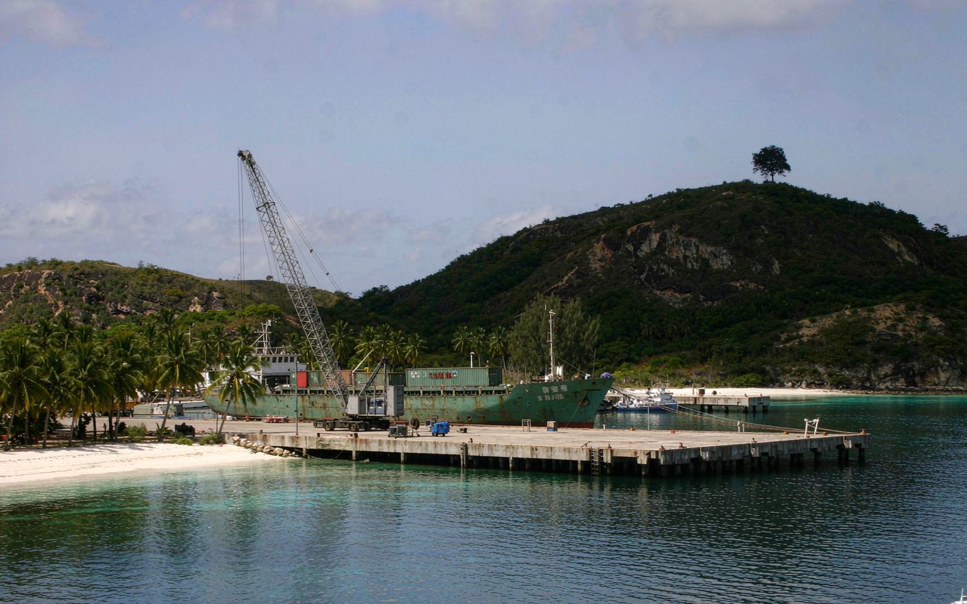 A container ship at a quay on a tropical lagoon island with turquoise water and green hills
