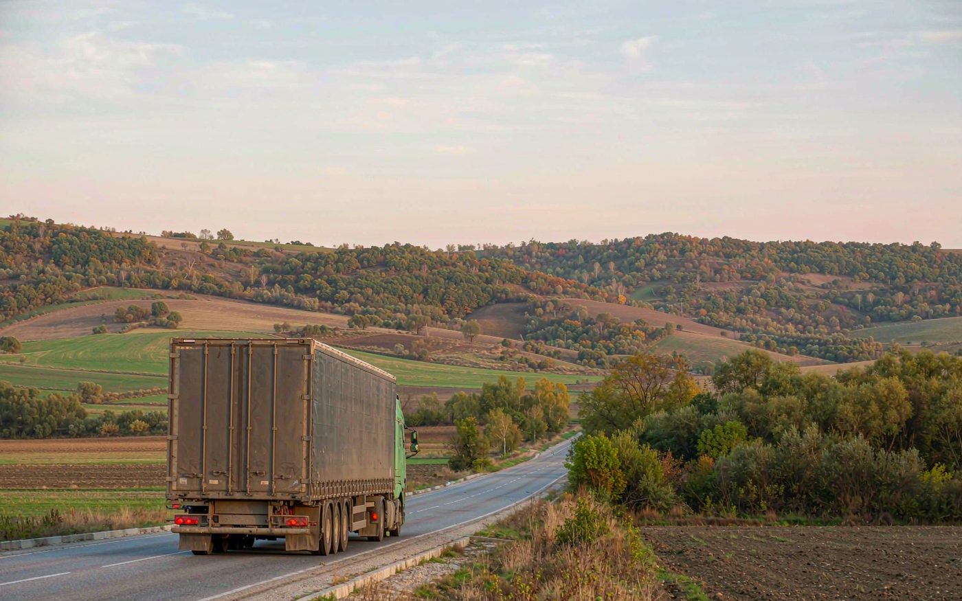 A container truck on a two-lane highway crossing the rolling farmland of Moldova