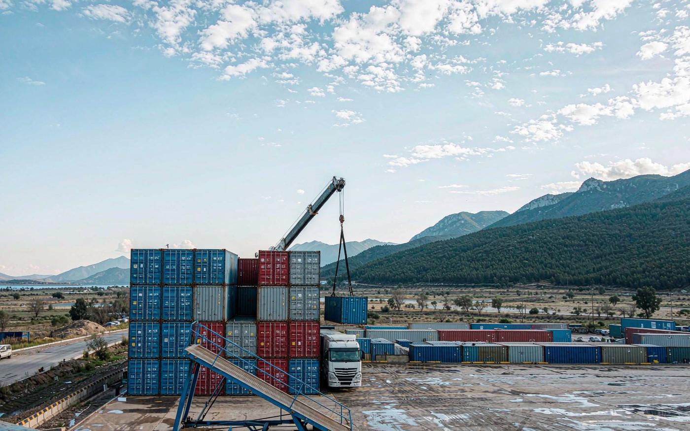 Containers at a Mediterranean seaport terminal with mountains inland, typical of the Thessaloniki routing