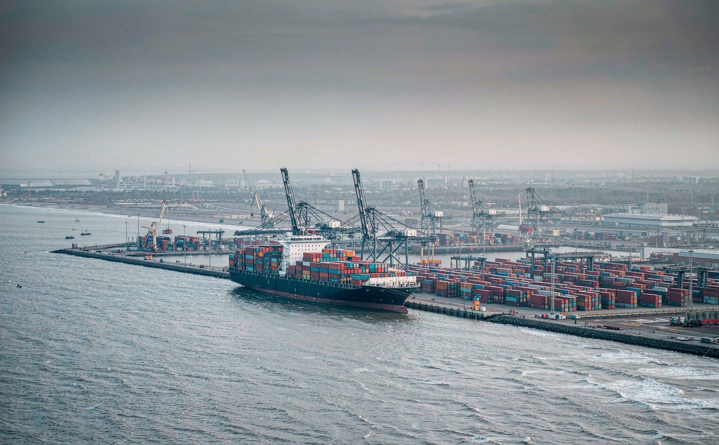 Deep-water container terminal on the Baltic coast in cold morning light, tall gantry cranes, stacked containers and a large container vessel moored at the quay
