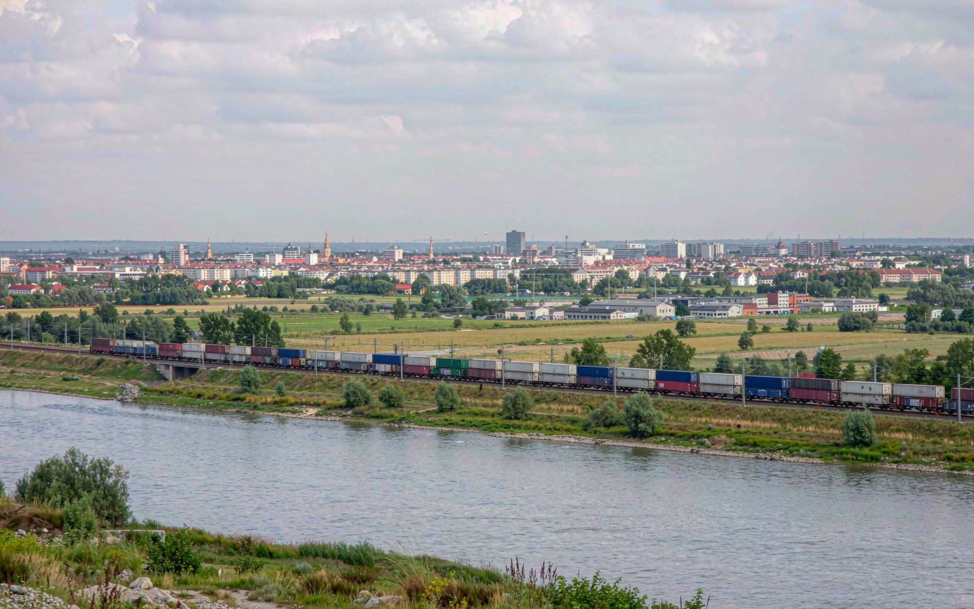 Freight train carrying containers through a broad river valley in the Balkans