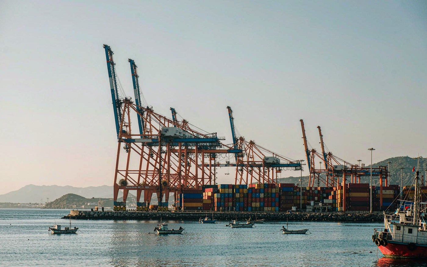 North African Mediterranean container port with gantry cranes, stacked containers and low hills behind