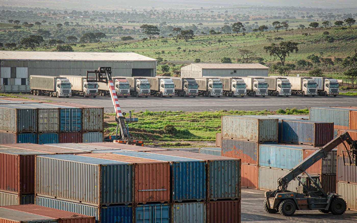 Inland container depot in East Africa with stacked shipping containers, a reach stacker and container trucks