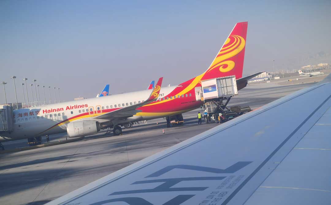 Aircraft parked at a Chinese airport apron with an airline in red and yellow livery, a loader at the forward door and a second aircraft behind