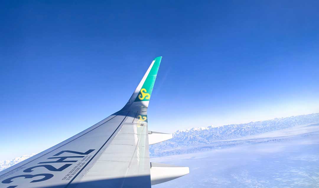 Aircraft winglet and wing seen from a passenger window above a band of cloud on a China to USA flight