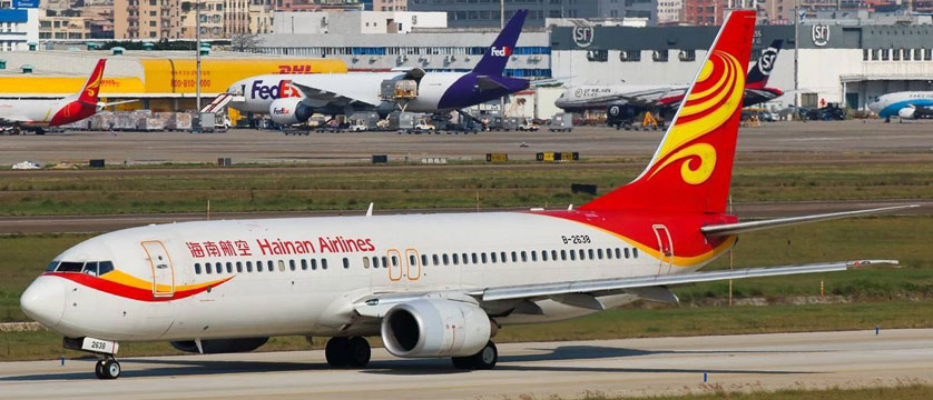 Chinese airline passenger aircraft in red and yellow livery on the apron with a second aircraft and terminal buildings in the background
