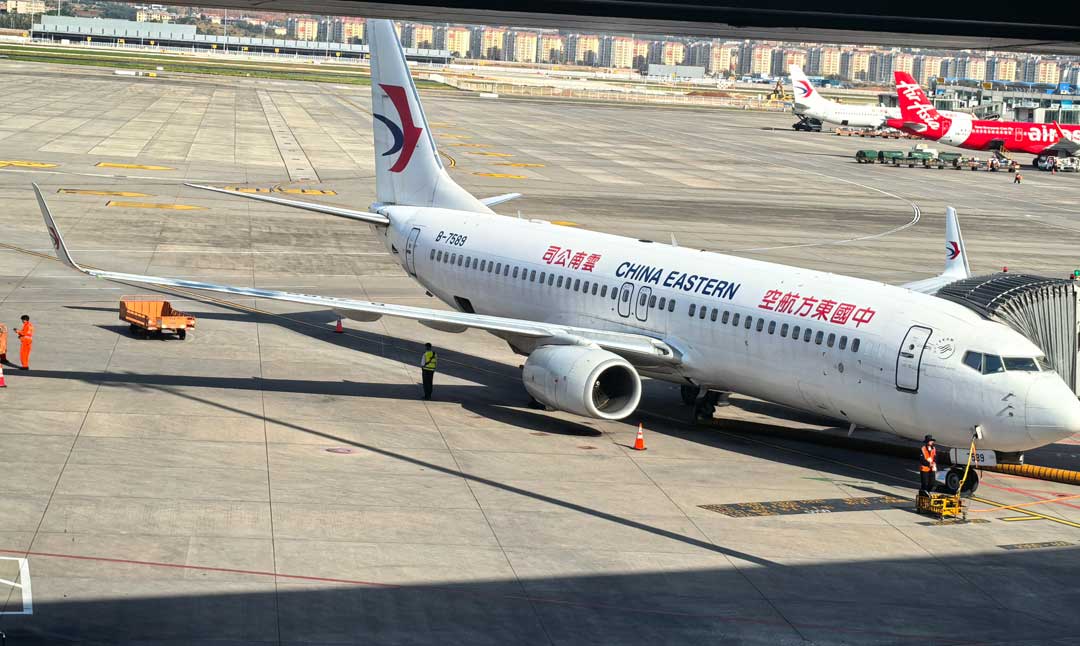 China Eastern Airlines passenger aircraft on the apron at a Chinese airport with ground service vehicles and terminal buildings behind