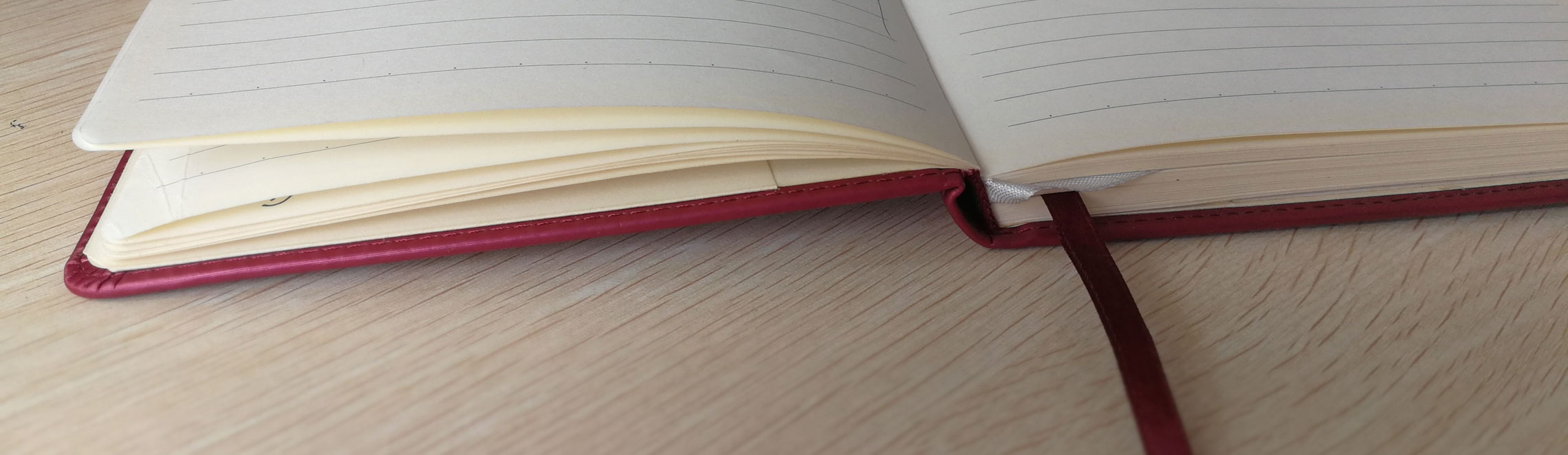 Open notebook with a red elastic band lying on a wooden desk next to a pen, representing export documentation preparation