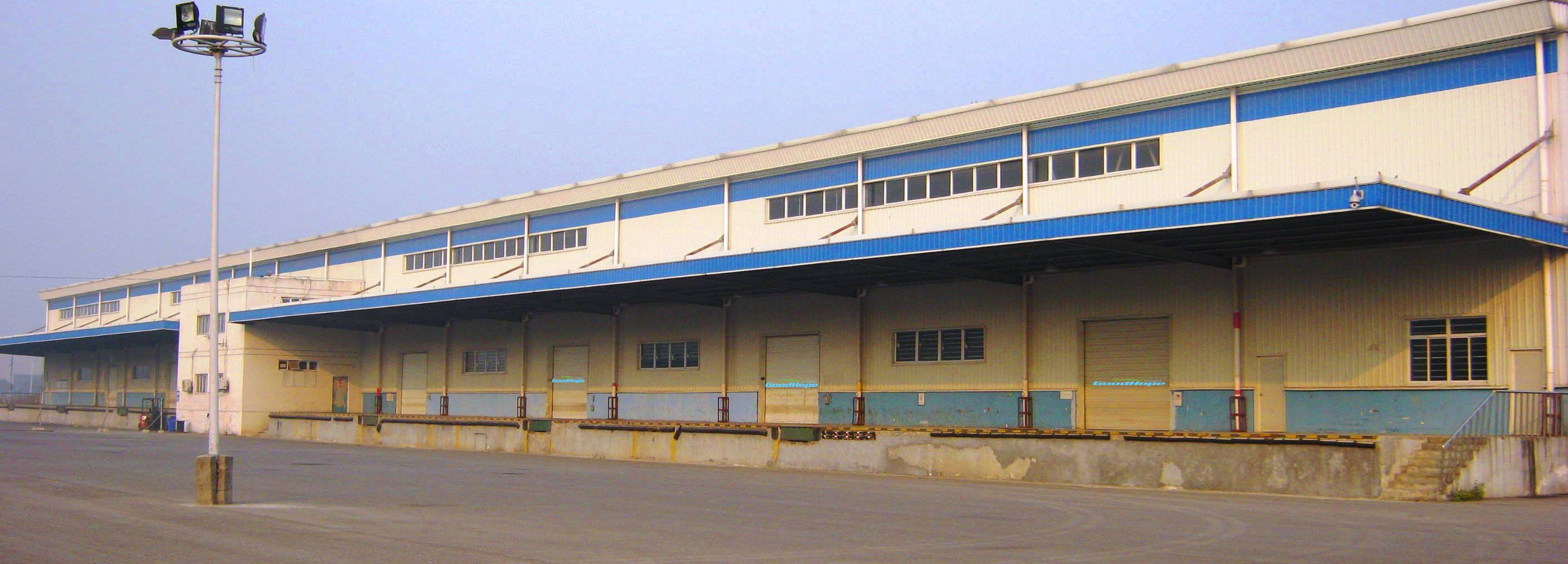 Long single-storey export warehouse in China with a blue roof trim and a wide empty concrete forecourt in front of the loading bays