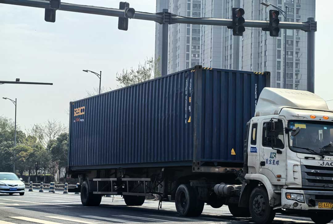 container truck hauling a blue container on a city road