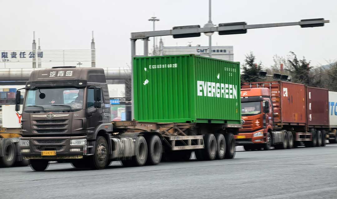 container truck hauling a green container on a port road
